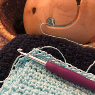 Crochet project with light teal yarn and crochet needle, yarn bowl, basket